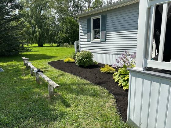 Curved mulch bed with new plantings beside a home in Newstead, NY