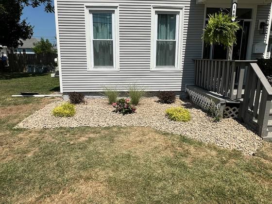 Stone bed with shrubs and grasses beside a front porch in Akron, NY